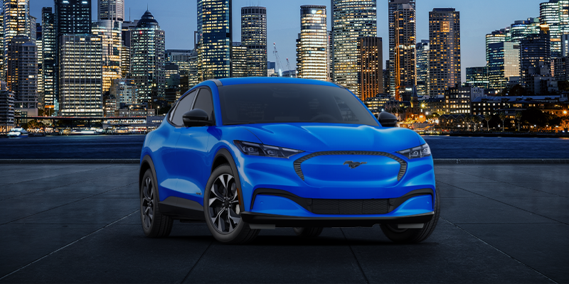 A blue Ford Mustang Mach-E electric vehicle with a city skyline in the background