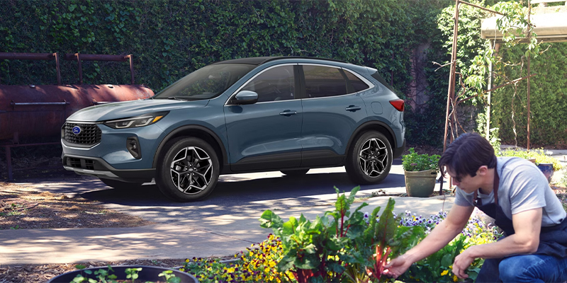 A Ford Escape parked in the driveway while the owner is in the garden in the foreground.